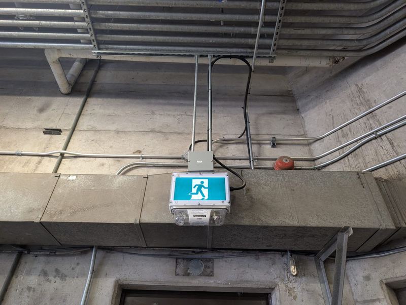 Illuminated exit sign installed with surface-mounted conduit in a concrete service area.