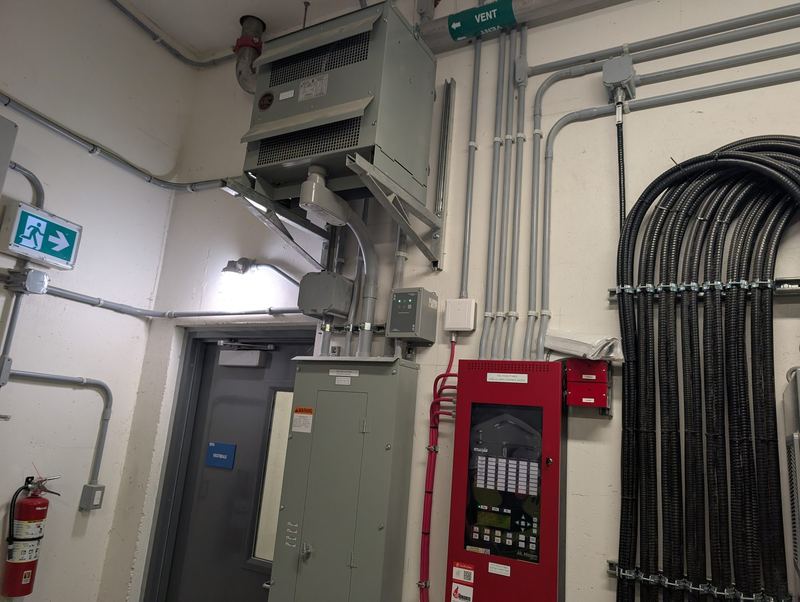 Fire alarm panel beside a power panel with a large neat bundle of flexible conduit runs.