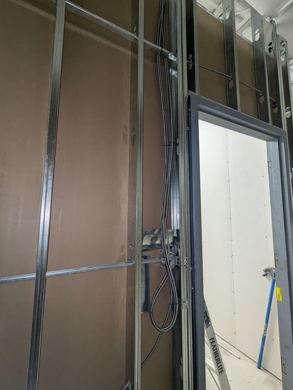 Steel-stud wall with EMT conduit and device boxes roughed in during a commercial fit-out
